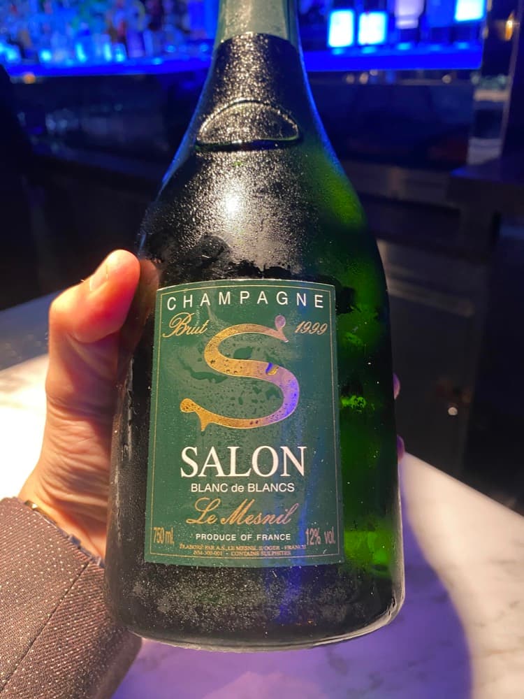 A bottle of Salon 1999 Blanc de Blancs Le Mesnil, held up in a dimly lit bar